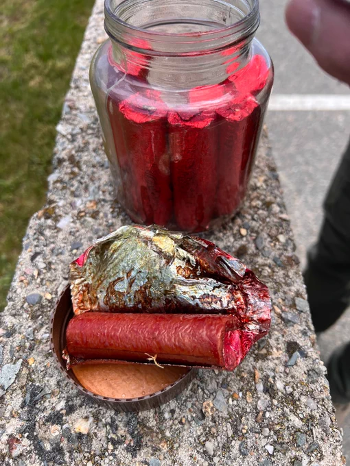 Glass jar filled with red cylinders placed on a stone ledge outdoors.