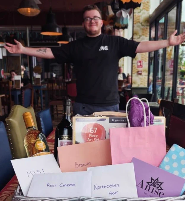 Image shows a man stood behind a hamper full of raffle prizes