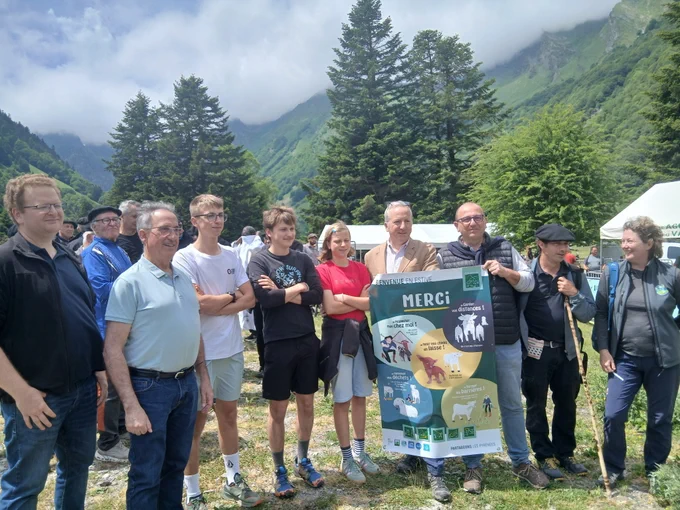 Photographie en plein air dans une vallée montagneuse verdoyante bordée par un lac d’un groupe qui se tient debout sur un chemin de terre et d'herbe. 