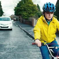 Image of child riding a bike on a road with a car approaching.