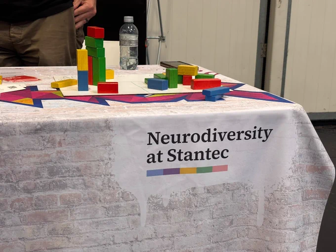 A table with a "Neurodiversity at Stantec" cloth, featuring colorful blocks scattered and stacked on it, alongside a water bottle and a phone.