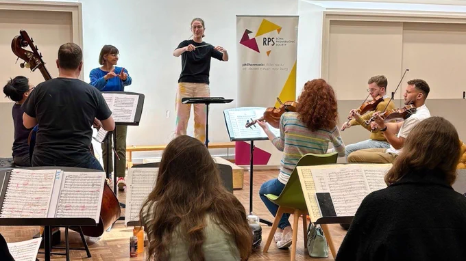 A participant at an RPS Conductors course, conducting an orchestra and receiving coaching from Alice Farnham.