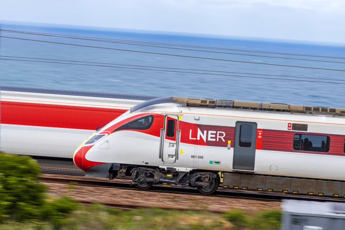 The end of an Azuma train emerging from the right with the sea visible behind, and a slice of its livery colours extending to the left