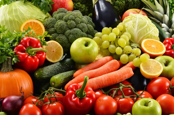 A colourful assortment of fresh vegetables and fruits including tomatoes, carrots, green apples, grapes, and broccoli.