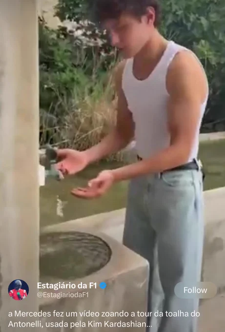 Kimi Antonelli, Mercedes F1 driver, wearing a white tank top and light wash jeans, washes his hands under an old outdoor stone fountain tap surrounded by greenery. Screenshot of a viral X post from Brazilian F1 account Estagiario da F1 joking that Mercedes made a video mocking Antonelli’s towel tour, the one used by Kim Kardashian.