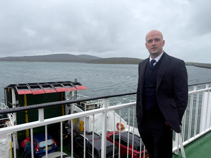 Transport Secretary Stephen Flynn poses for a photo on the viewing deck of the MV Loch Portain. Western Isles scenery in the background.
