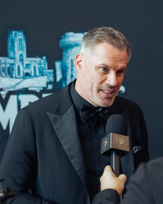 A man in a black tuxedo is being interviewed at a formal event. The mood is professional and engaging.