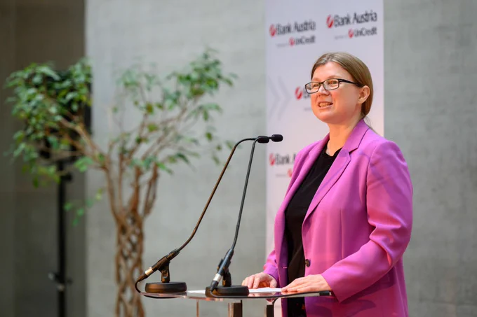Eine Frau in einem rosa Jackett steht an einem Rednerpult und hält eine Rede.