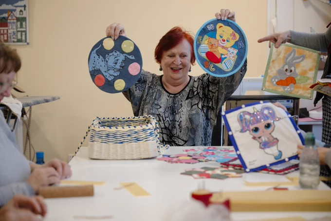 A participant proudly displays handmade textile crafts during a creative workshop at the Leisure and Social Services Centre for Older People in Synelnykove. The centre offers sewing and handicraft activities that bring together older adults and displaced residents.