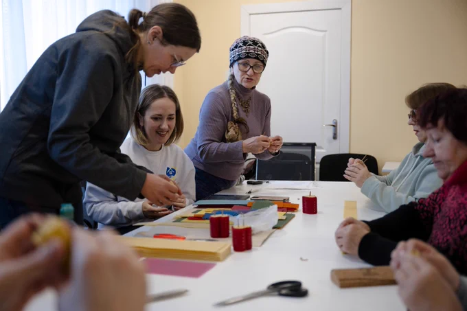 Participants and facilitators collaborate during a handicrafts workshop at the Leisure and Social Services Centre for Older People in Synelnykove. The centre provides a welcoming space where local residents and internally displaced people can learn new skills, socialize, and support one another.