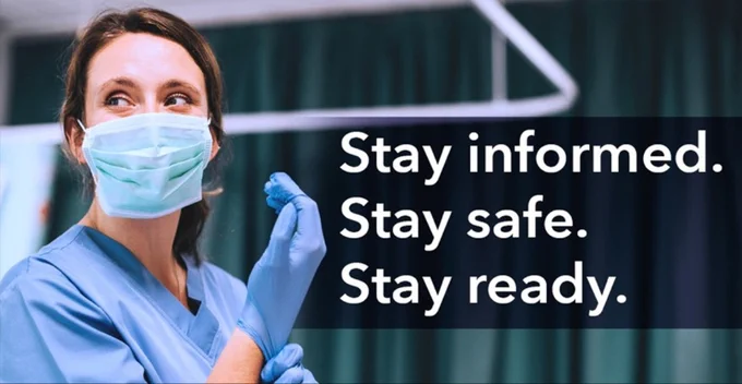 A healthcare worker in blue scrubs and mask is pulling on a pair of blue gloves. Stay informed, stay safe, stay ready.