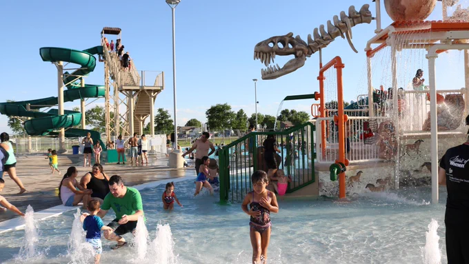 Families play at Discovery Bay Waterpark, with a slide ane dinosaur theme dump bucket. 