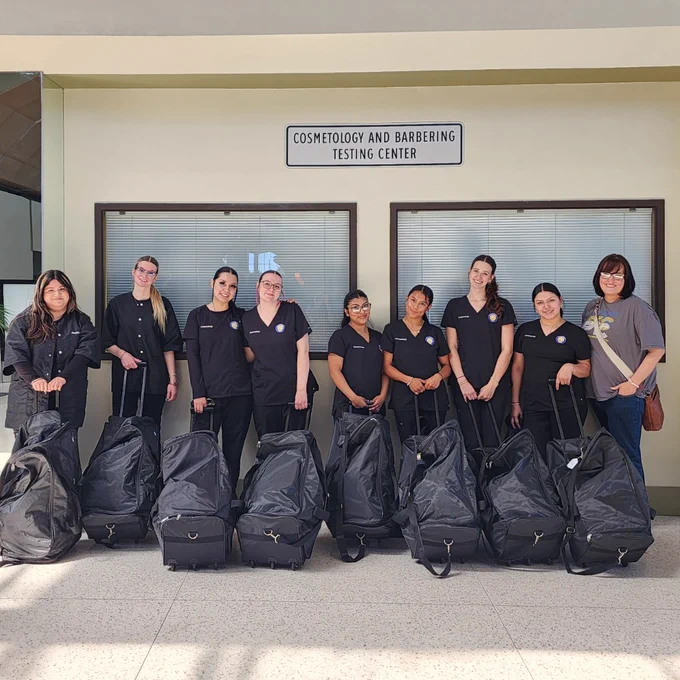 Group of nine cosmetology and barbering students standing with large black bags outside the testing center entrance.