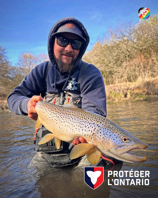 Matthew debout dans une rivière en tenant une truite brune.