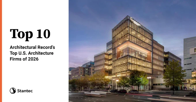 Modern multi-story office building illuminated at dusk in an urban setting with surrounding cityscape and light trails from passing cars.