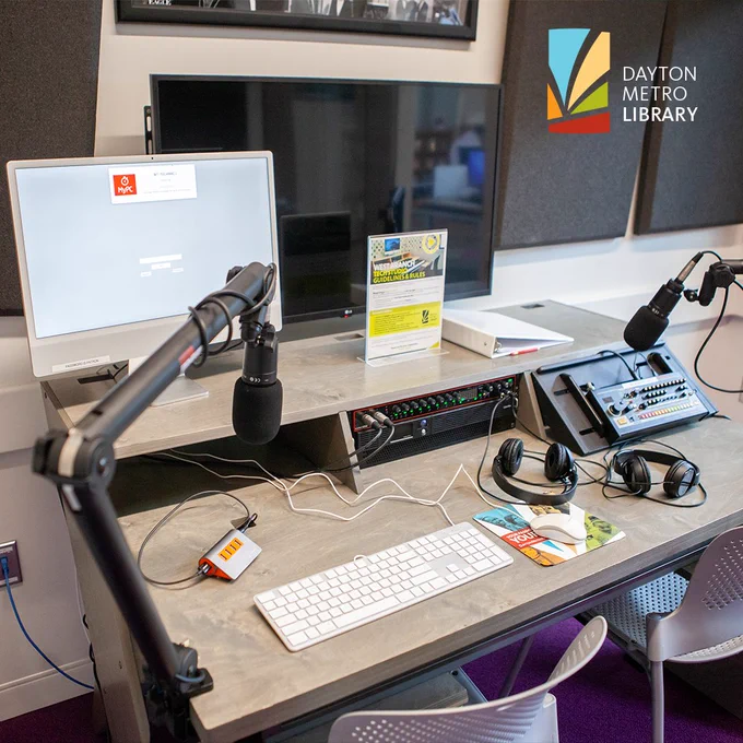 Audio workstation with computer monitors, microphones, headphones, and a sound mixer arranged on a desk in a library recording studio.