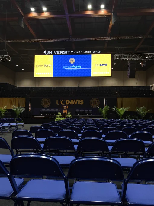 Rows of empty chairs facing the UC Davis Graduate Studies commencement stage inside the Credit One Union Center.