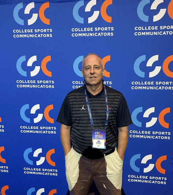 Jim McCurdy standing against the College Sports Communicators backdrop.