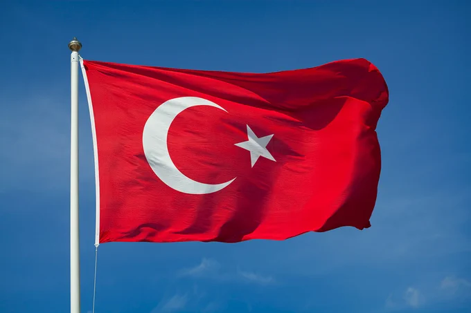 Red Turkish flag with a white star and crescent waving against a clear blue sky.