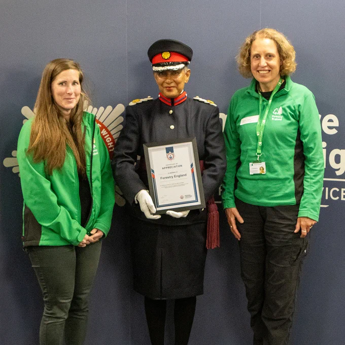 Three people standing at a certificate presentation, including two members of Forestry England standing either side of an officer from the Hampshire and Isle of Wight Fire and Rescue Service.