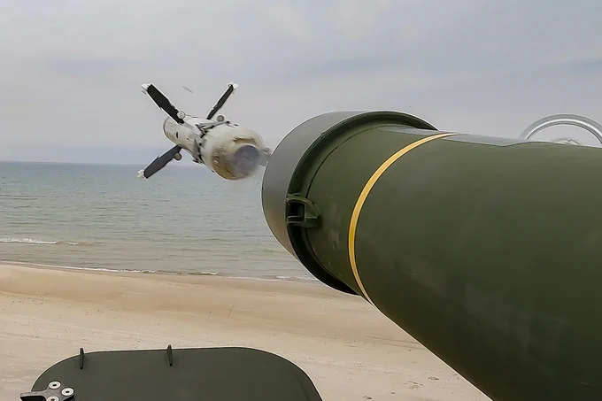 Close-up of a missile launching from a green military launcher on a beach with the ocean in the background.