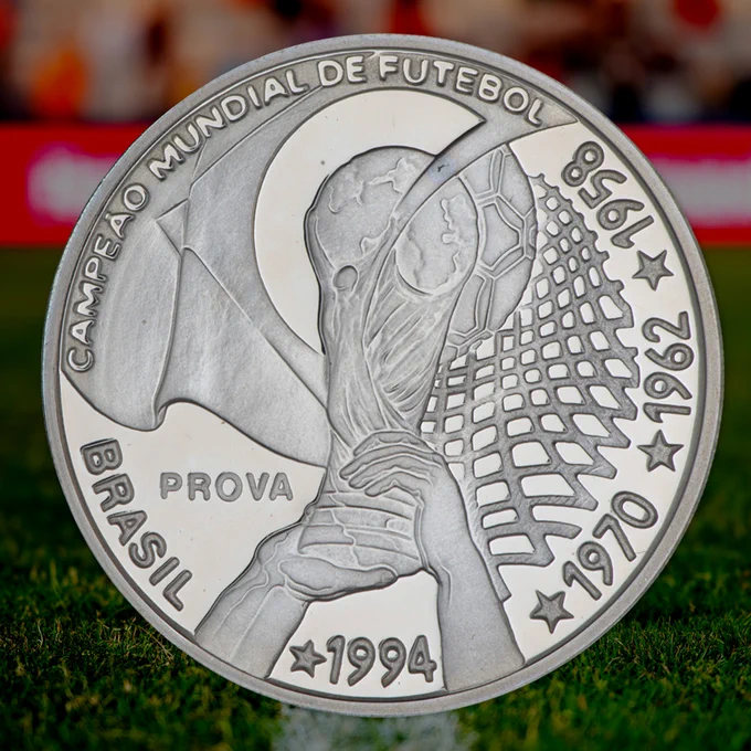 Pièce commémorative montrant le trophée de la Coupe du monde de la FIFA. On y voit le texte « CAMPEÃO MUNDIAL DE FUTEBOL » et « BRASIL », ainsi que les chiffres 1958, 1962, 1970 et 1994, soit les années où le Brésil a remporté la Coupe. Le mot « PROVA » est aussi visible.
