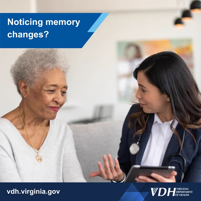 Senior woman discussing memory concerns with a healthcare professional holding a tablet in a home setting.