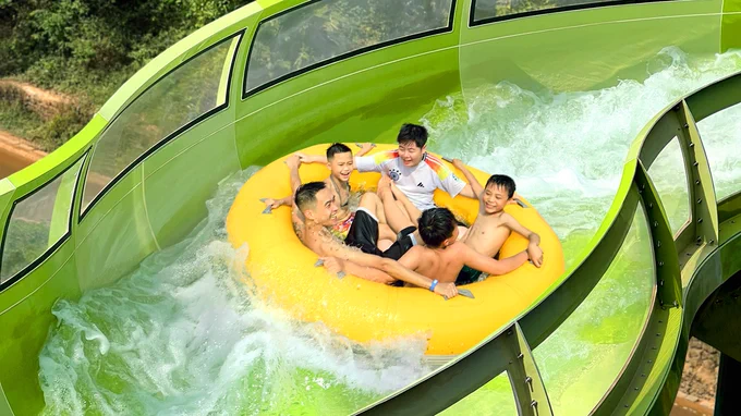 People on a yellow raft sliding down a curvy green water ride named PowerRAPIDS at Aquatopia Water Park in Vietnam.