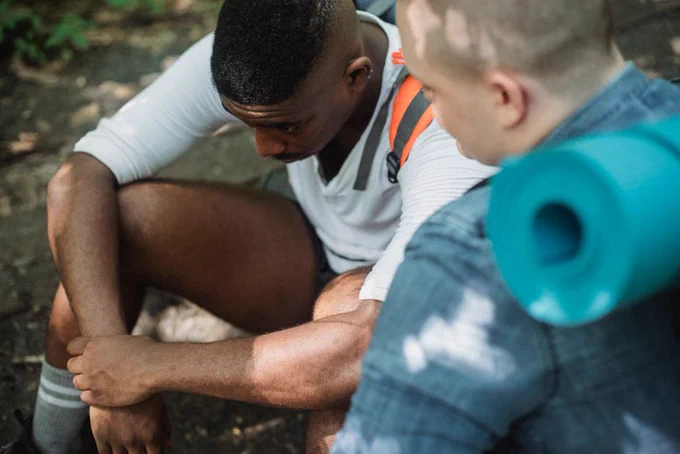From above of tired African American male hiker having break in trekking with friend in woods