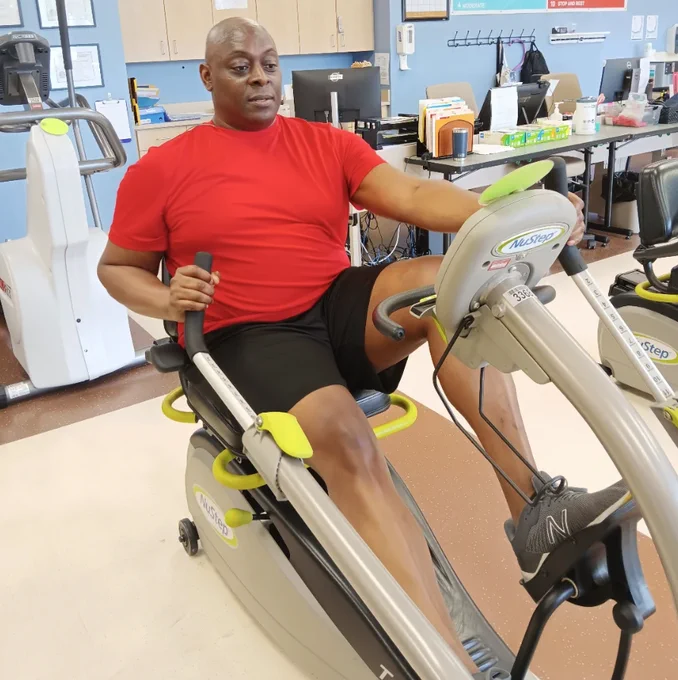 Man exercising on a NuStep T4r recumbent cross trainer at a cardiac rehabilitation facility, engaging in low-impact, full-body movement to support heart health, strength, and recovery in a clinical setting.