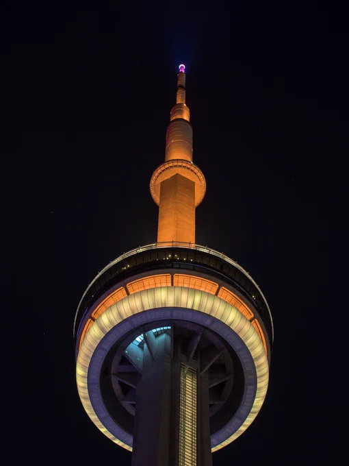 Closeup of the CN Tower at night lit orange and yellow / Gros plan de la Tour CN illuminée en orange et jaune la nuit 