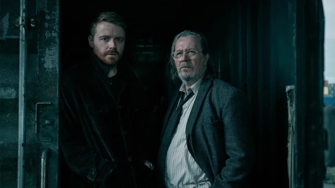 characters river cartwright and jackson lamb (played by jack lowden and gary oldman respectively) pose in front of a shipping container