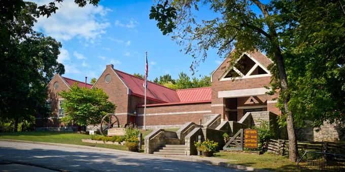 Brick building with a red roof surrounded by trees and a flagpole in front under a blue sky.