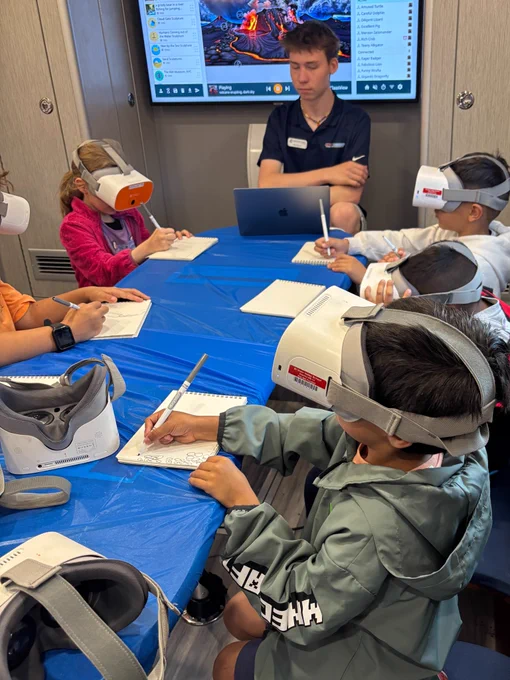 Students use virtual reality headsets, markers, and sketch books on a blue table during the Mobile Innovation Lab visit to Estes Park Elementary.