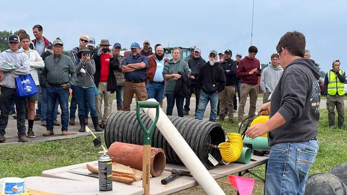 A person demonstrating tools to a large group outdoors under a cloudy sky.