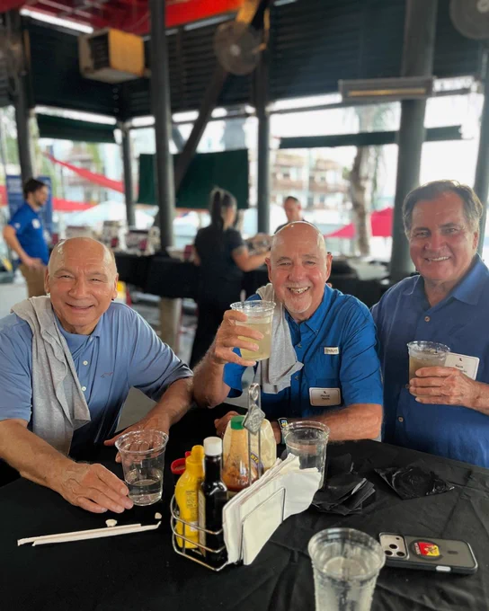 Three men smile while seated a table holding drinks.