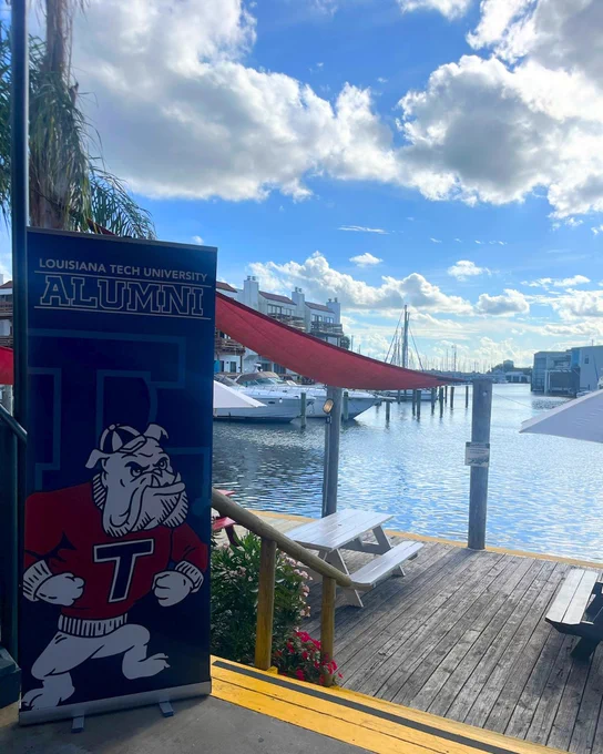 A vertical Louisiana Tech alumni banner is displayed on a patio overlooking a marina