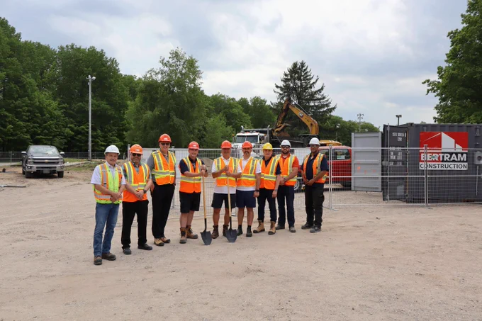 Council, staff, and representatives from Bertram Construction posing for a photo at the groundbreaking of the Toanche Pavilion in Toanche Park. Heavy equipment is behind them inside the gated area.