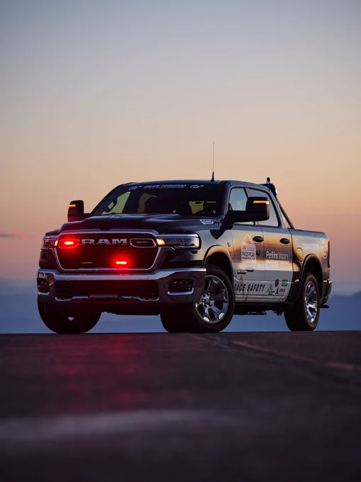 A RAM truck with visible safety markings and illuminated red lights is parked during sunset. The calm evening sky adds a serene backdrop.