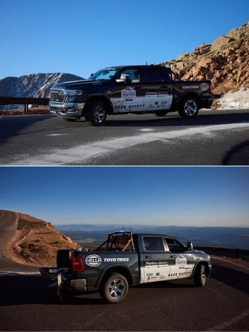 A safety truck on a winding mountain road during sunrise, adorned with various sponsor logos. The scene suggests preparation for a racing event at Pikes Peak.