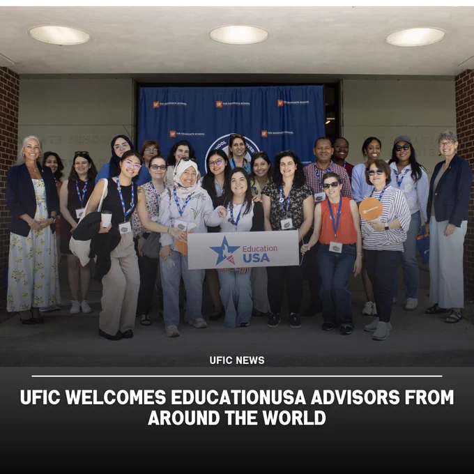 Group of diverse EducationUSA advisors posing together outside a building, holding a sign with the EducationUSA logo.