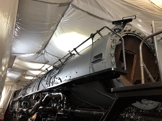A large, freshly painted steam locomotive inside a tent. The locomotive's front is open. 