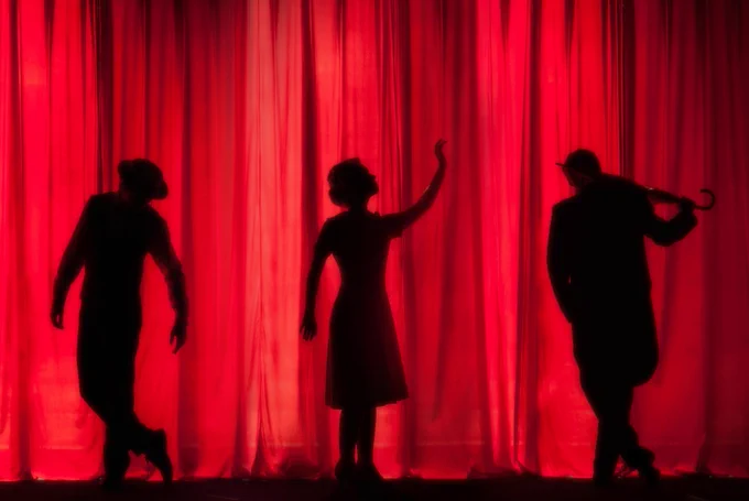 Stage curtain with three human figures in silhouette from Unsplash