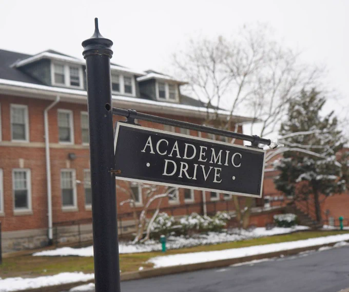 Photo of a street sign that reads “Academic Drive” in front of a snowy street and red brick building.