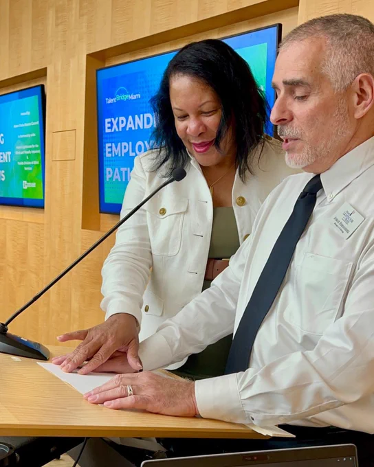 (Photo) Dr. Paula Hopkins, Executive VP of Strategic Partnerships and Funding Development at Beacon Council and Jorge Hernandez, Miami Lighthouse Manager of Technology, share a podium, speaking into a microphone during their presentation.
