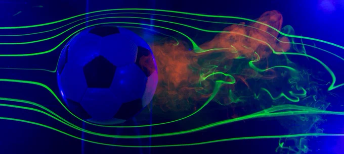 Bright green lines of vapor bend and swirl around a soccer ball during aerodynamics testing in a wind tunnel