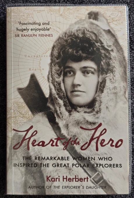 Front cover of this softback book shows a close up section of a sepia coloured photograph of the Victorian female arctic explorer Jo Peary, dressed a hooded fur coat which was the arctic clothing of the time. Overlaid on this image is the title of the book in burgundy lettering 'Heart of a Hero, the remarkable women who inspired the great polar explorers', by Kari Herbert.