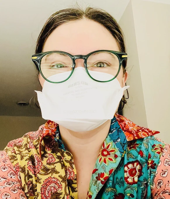 I'm wearing a colorful patchwork button down shirt, green frame glasses, and a white duckbill n95 mask.