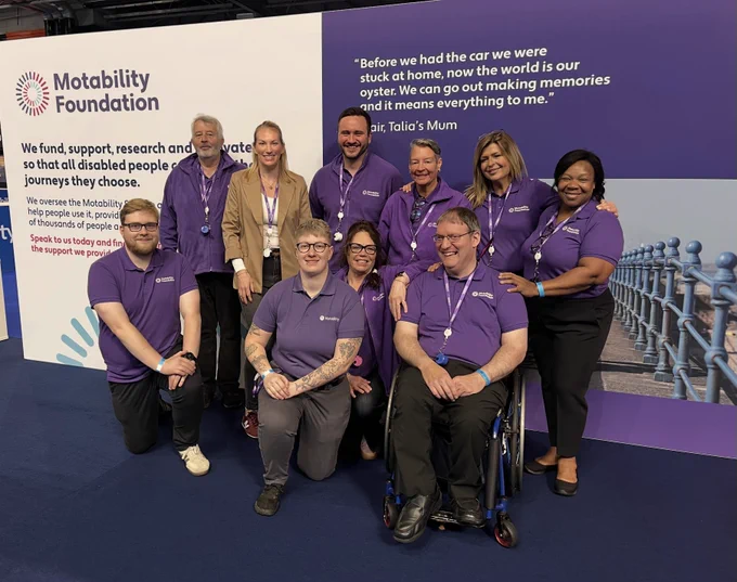 A group of Motability Foundation colleagues are posing in front of a branded Motability Foundation stand at the Motability Scheme Live event. They are all facing the camera and smiling.

In the back row is Ian, Katie, Will, Tracie, Claire and Dawn and in the front way is Tom, Rae, Cheryl and Barry.