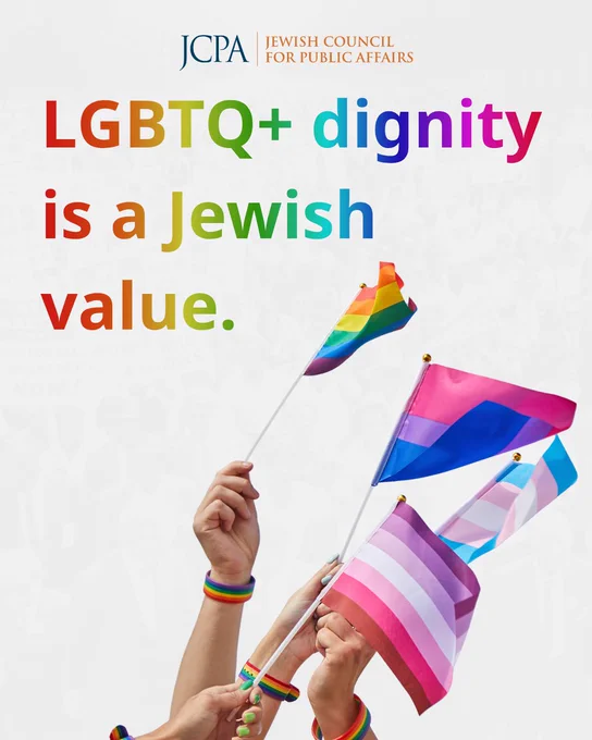 Pride Month graphic featuring the message “LGBTQ  dignity is a Jewish value” in large rainbow-colored text on a light gray background. At the bottom, several hands wearing rainbow wristbands hold Pride, bisexual, transgender, and lesbian pride flags. A faint image of a civil rights march appears in the background, and JCPA branding is displayed at the top.